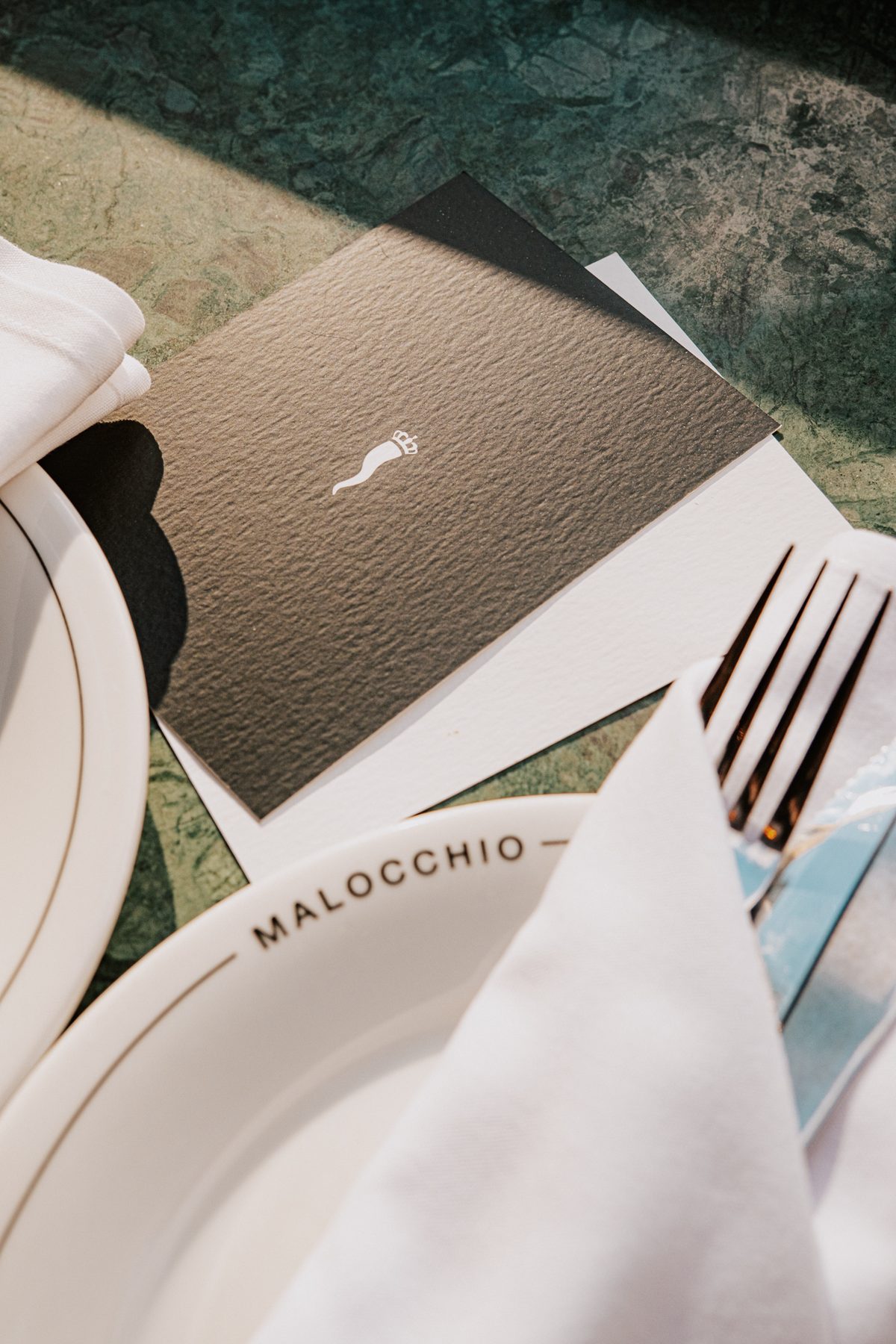 A Malocchio table laid with the corno card, plates and cutlery on green marble