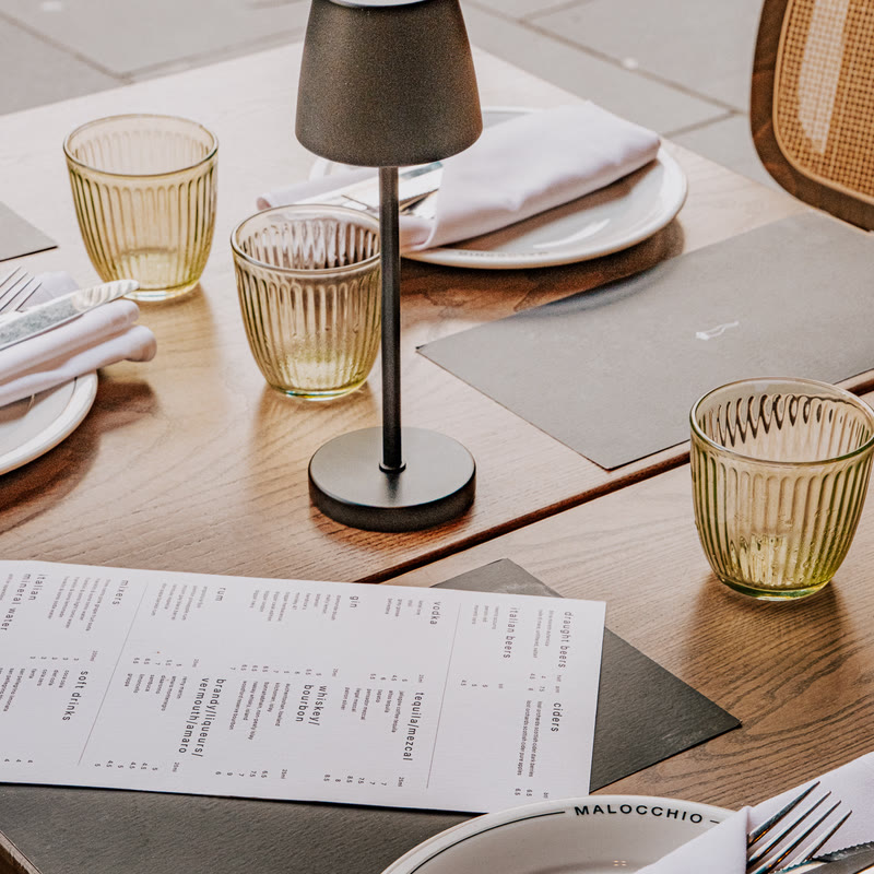 A table laid up with the drinks menu, ribbed green tumblers and a table lamp